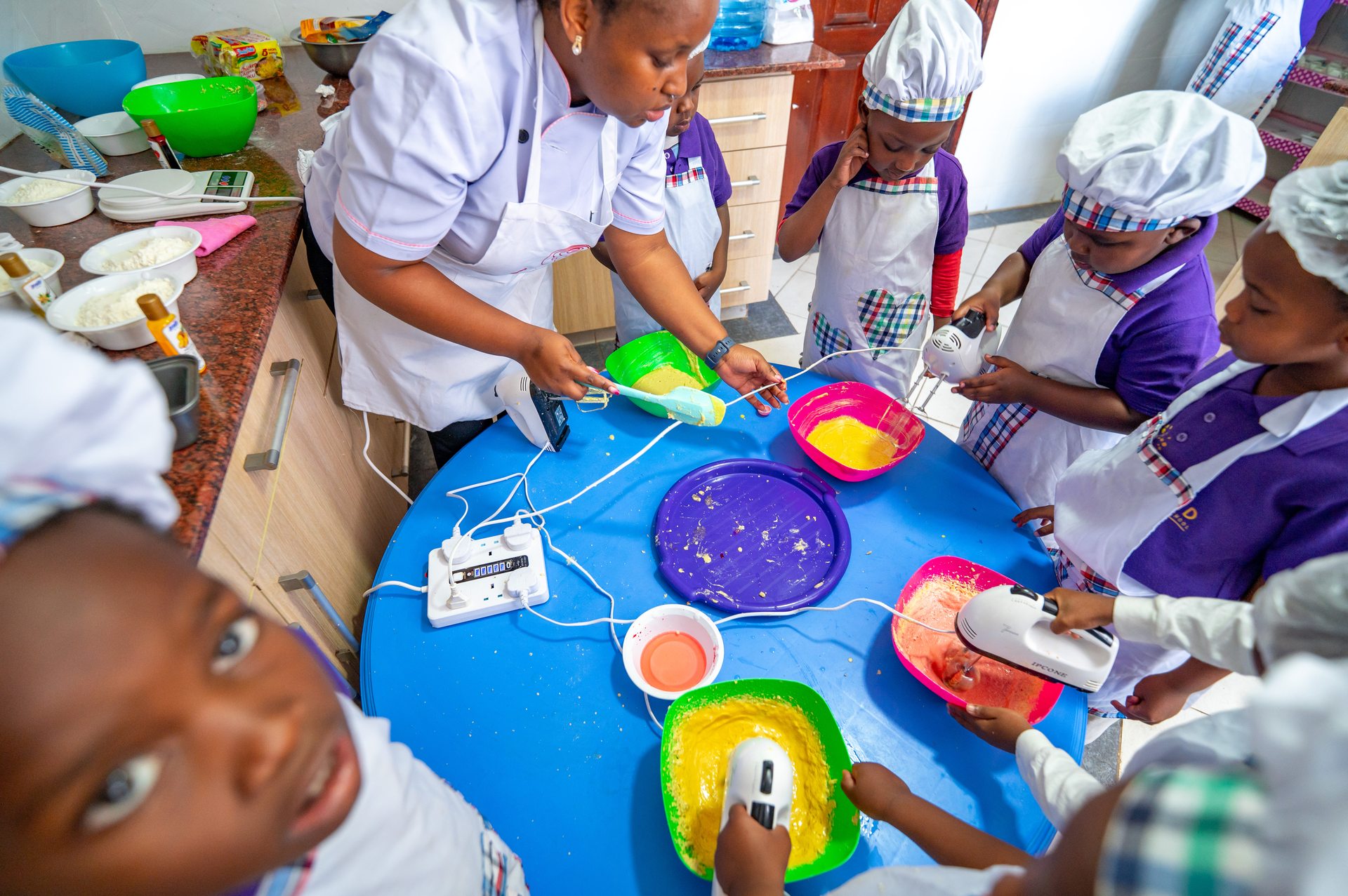 Children in chef hats baking together with their teacher